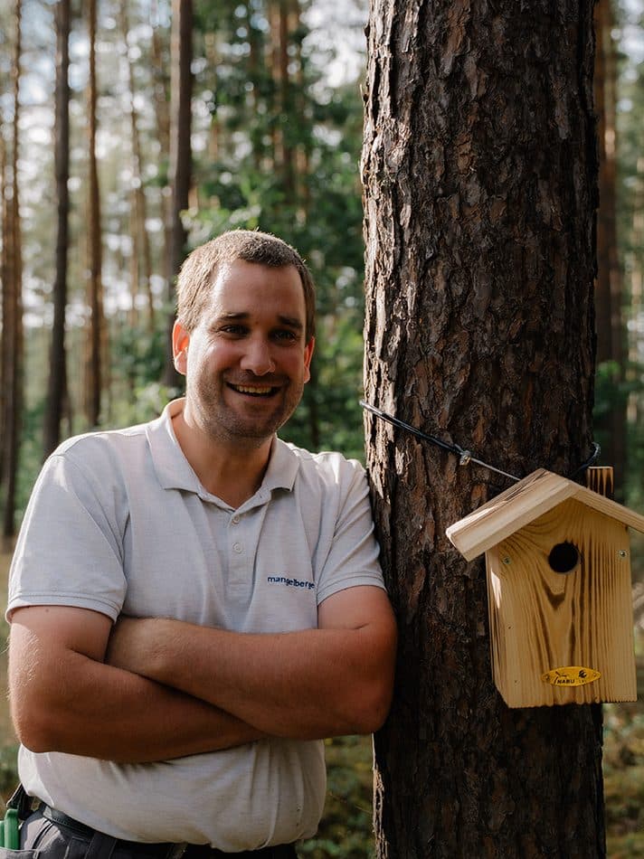 Mangelberger-Mitarbeiter an einem Baum mit Vogelhaus auf dem Firmengelände